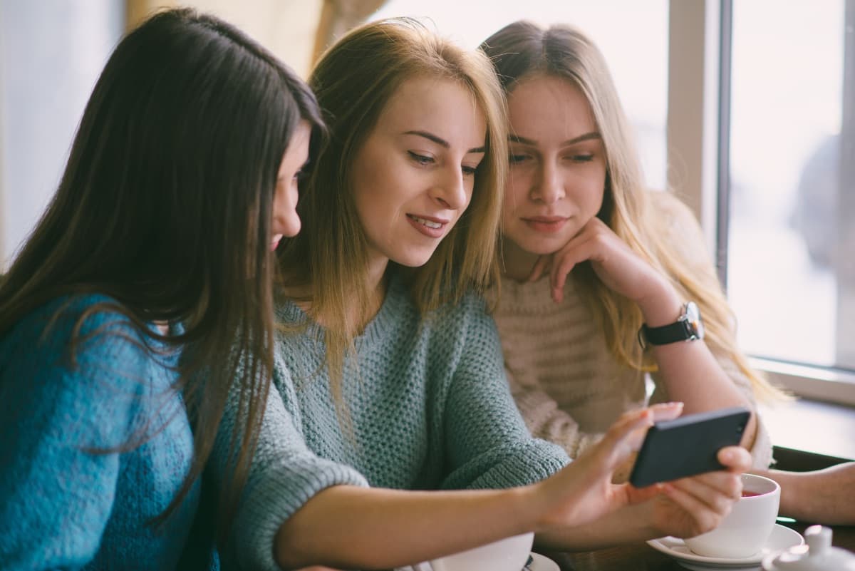 Drei junge Frauen schauen in einem Café gemeinsam auf ein Smartphone