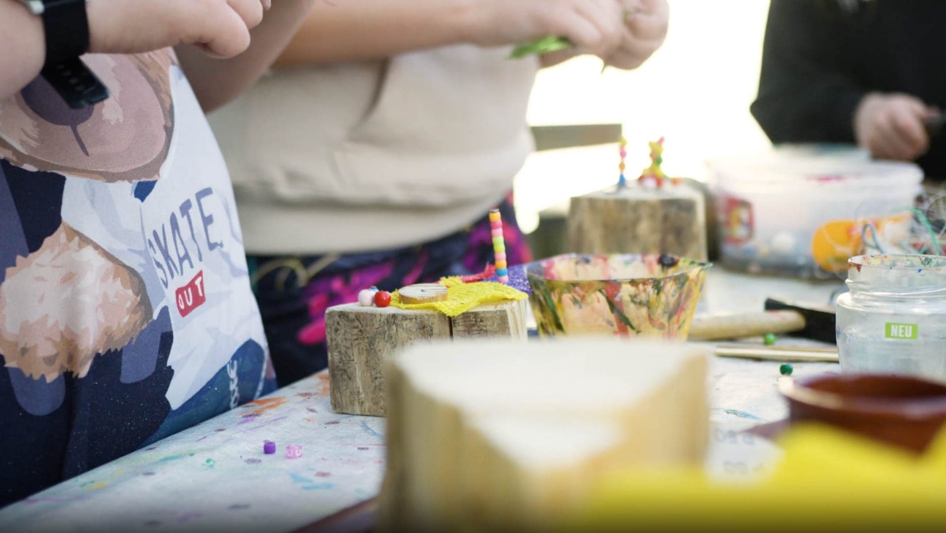 Kinder gestalten gemeinsam an einem Tisch mit Holz, Perlen und buntem Material als Symbol für die soziale Gruppenarbeit